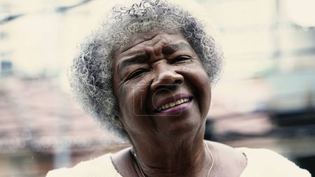 Photo for One South American Senior woman in 80s smiling at camera standing outside in drizzle rain. Portrait of an elderly black lady with gray hair - Royalty Free Image