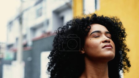 Foto de Creyendo que la mujer afroamericana siente la presencia de un poder superior, inspiró Skyward Close-Up Face mirando hacia arriba en el entorno urbano. Una joven contemplativa negra teniendo ESPERANZA - Imagen libre de derechos