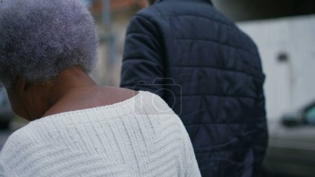 Foto de Señora mayor afroamericana paseando por la calle con la ayuda de su hijo adulto de mediana edad cuidador, caminando hacia adelante en el seguimiento de tiro wiht movimiento en el entorno urbano - Imagen libre de derechos
