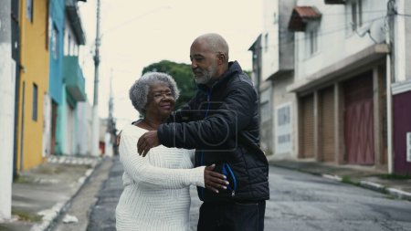 Foto de Abrazo amoroso del hijo afroamericano con la madre anciana en City Street, cuidado genuino entre los 80 y su cuidador - Imagen libre de derechos