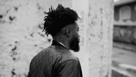 Ein aggressiver afroamerikanischer junger Mann schlendert durch die urbane City Street, monochrome Schwarz-Weiß-Spurensuche