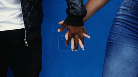 One black couple joining hands together on blue city wall backdrop. African American man and woman united, caring supportive relationship