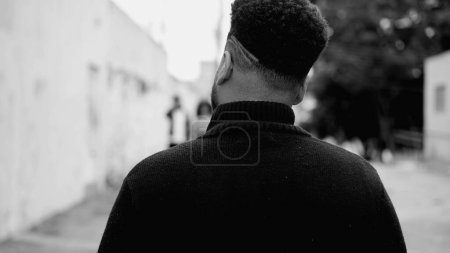 Téléchargez les photos : Dos de jeune homme marchant en milieu urbain en noir et blanc, monochromatique. Un noir sud-américain se promène dehors - en image libre de droit