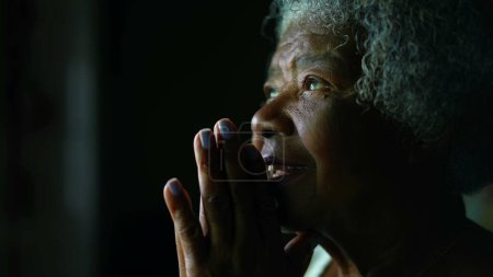 Foto de Fiel y espiritual Senior mujer afroamericana con el pelo gris abriendo los ojos sintiendo GRATULA mientras ORA a DIOS. Una anciana religiosa en los años 80 cara de cerca - Imagen libre de derechos
