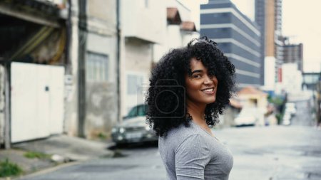 Selbstbewusste Frau afrikanischer Abstammung, die in der urbanen südamerikanischen Stadt spaziert, eine lockige schwarze Frau, die Freude und Ermächtigung ausstrahlt