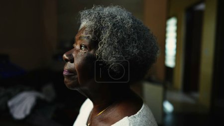 Close-up face of a Senior African American woman staring at window indoors in solitude. One thoughtful pensive older black lady with gray hair in contemplation