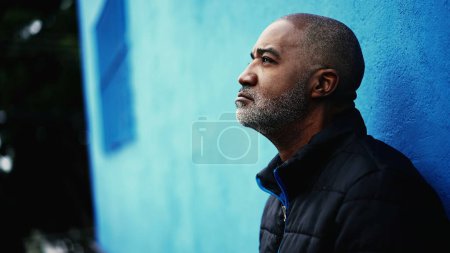 Photo for One pensive middle-aged black man standing outside in city street gazing upwards in deep contemplative expression. Thoughtful look of an African American person in 50s - Royalty Free Image