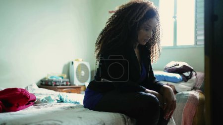 Photo for Concerned African American woman seated by bedside looking down with pensive worried gaze, a black middle-aged latina struggling with mental reflection during challenging times - Royalty Free Image