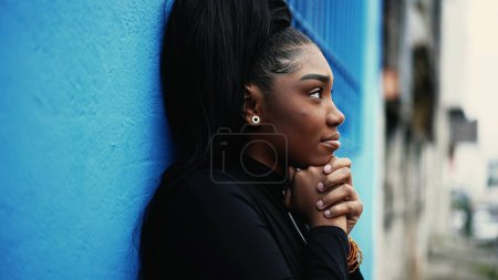 Photo for One hopeful young black woman gazing upwards with FAITH and GRATITUDE standing outside in city street. African American adult girl looking UP smiling in urban environment - Royalty Free Image