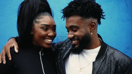 Téléchargez les photos : Heureux jeunes afro-américains riant et souriant, un homme noir avec le bras autour de la soeur interaction authentique debout sur le mur bleu dans l'environnement urbain, portraits vibrants - en image libre de droit