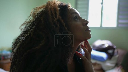 Photo for Pensive South American latina woman in 50s pondering decision at home contemplating life during challenging times seated by bedside - Royalty Free Image