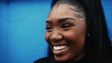 Foto de Una joven hispana negra sonriendo en la pared azul, cara de cerca de una chica milenaria de 20 años de ascendencia africana con expresión feliz - Imagen libre de derechos