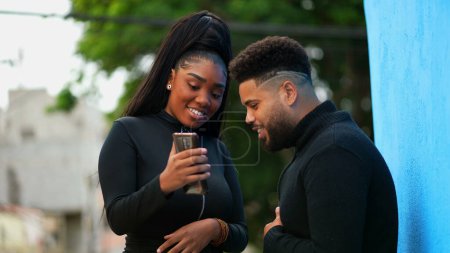 Adult Girl Sharing Cellphone Screen with Male Friend standing outside urban sidewalk. Candid people looking at content online together. Woman shares media by holding phone