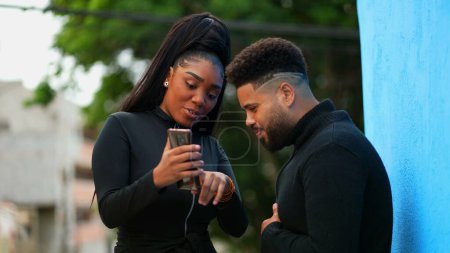 Adult Girl Sharing Cellphone Screen with Male Friend standing outside urban sidewalk. Candid people looking at content online together. Woman shares media by holding phone