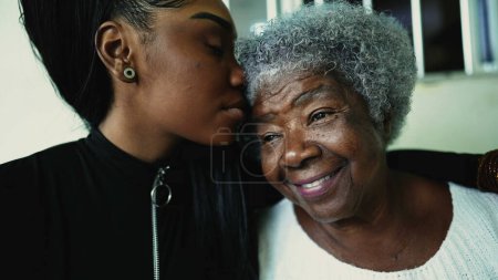 Caring granddaughter kisses elderly 80s grandmother in forehead in sign of deep love and support of inter-generational family moment. African American individuals