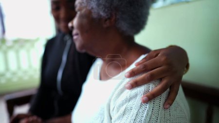 Photo for African American granddaughter caring for elderly grandmother in old age with arm around shoulder showing help and support for senior woman in 80s, inter-generational family care - Royalty Free Image