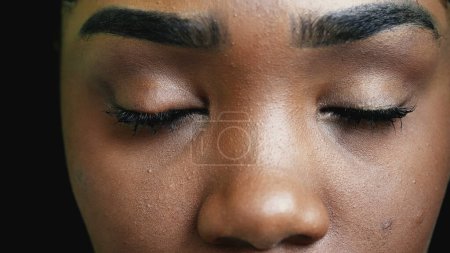 Foto de Una joven negra cerrando los ojos en meditación, una chica adulta afroamericana practicando mindfulness, abre los ojos al cielo en macro detalle de primer plano sonriendo - Imagen libre de derechos
