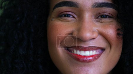 Photo for One joyful brazilian black latin woman macro close-up face smiling at camera. Curly hair adult girl in 20s feeling happy, wearing make-up - Royalty Free Image