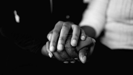 Caring for the eldrly - close-up detail of holding hands in dramatic black and white. Younger hand wrapped around an elderly wrinkled hand showing support and help