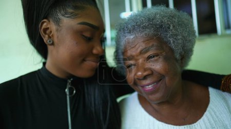 Photo for African American Granddaughter holding grandmother's hands and caring embrace showing love and support at family member in old age, teen girl kisses grandma's forehead - Royalty Free Image