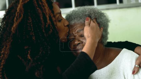 Photo for Tender loving moment of African American adult daughter kissing elderly 80s senior mother in the forehead and posing close-up faces smiling at camera - Royalty Free Image
