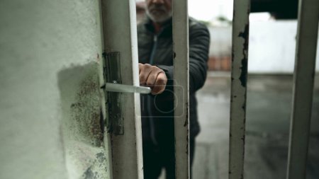 Photo for One senior black man steps inside residence home, opening front gate at urban sidewalk street. South American 50s person of African descent arrives from walk during daily routine - Royalty Free Image