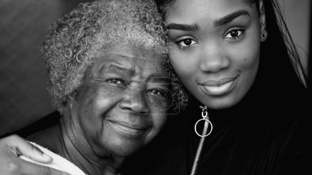 Porträt einer schwarzen Enkelin mit ihrer betagten Großmutter aus den Achtzigern, die das Alter zwischen zwei Generationen in monochromen Farben gegenüberstellt. Porträt afroamerikanischer Familienmitglieder in Schwarz-Weiß