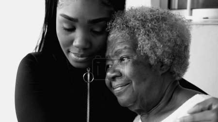 Téléchargez les photos : Petite-fille afro-américaine embrassant la grand-mère âgée aînée sur le front en noir et blanc, monochrome. Amour tendre et affection entre les membres de la famille intergénérationnelle - en image libre de droit