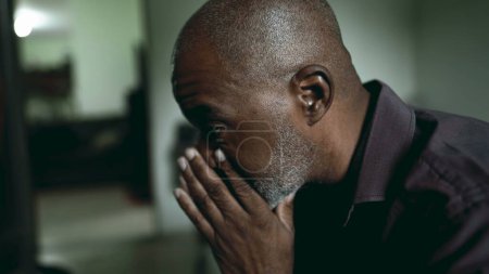 Photo for One depressed senior man covers face in shame and regret in moody gloomy bedroom. African American person struggles with poverty and mental illness, close-up face feeling hopeless - Royalty Free Image