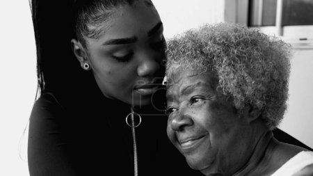 Photo for African American grandaughter kissing senior elderly grandmother in forehead in black and white, monochrome. Tender love and affection between inter-generational family members - Royalty Free Image