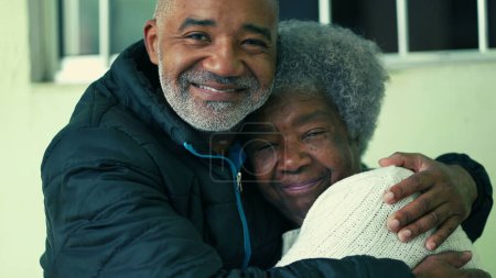 Téléchargez les photos : Adulte noir sud-américain d'âge moyen fils embrassant la mère âgée de cheveux gris des années 80 dans un câlin tendre aimant représentant les soins et le soutien dans la vieillesse - en image libre de droit