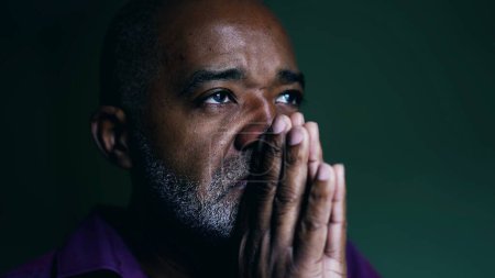 Photo for Spiritual African American senior person praying to GOD, closing eyes in contemplation with hands clenched together. Faithful man asking for HELP and SUPPORT - Royalty Free Image