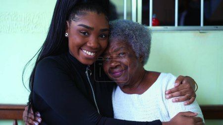 Photo for South American black granddaughter hugging her elderly grandmother portrait in tender inter-generational love and affection. Teen girl caring for senior woman - Royalty Free Image