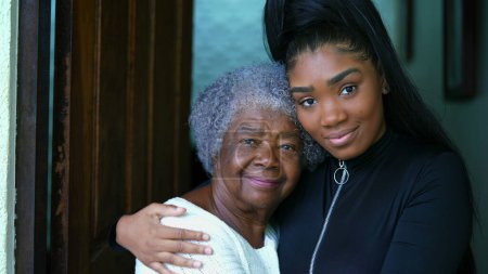 Téléchargez les photos : Afro-américaine grand-mère et petite-fille montrant le contraste d'âge, jeune femme avec bras autour des années 80 dame âgée dans le moment attentionné et tendre entre le lien intergénérationnel - en image libre de droit