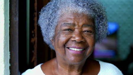 Photo for One happy black South American elderly lady in 80s of African descent smiling at camera. Portrait of a Gray-hair lady with wrinkles and joyful expression standing at residential home - Royalty Free Image