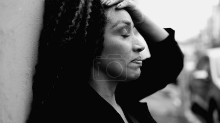 Foto de Afectada mujer afroamericana de mediana edad que sufre en la desesperación tranquila al aire libre en el entorno urbano, persona que lidia con la ansiedad mental, luchando con la vida moderna, blanco y negro - Imagen libre de derechos