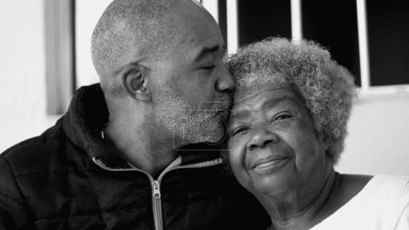 Foto de Momento tierno cariñoso del hijo adulto de 50 años besando a la anciana madre de 80 años en la frente, Retrato de personas intergeneracionales sudamericanas de ascendencia africana en monocromo, blanco y negro - Imagen libre de derechos