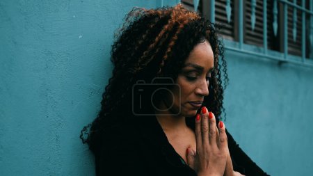 Foto de Mujer latina hispana preocupada de mediana edad de ascendencia africana en oración en ambientes urbanos afuera buscando esperanza y ayuda durante tiempos difíciles en profunda contemplación mental - Imagen libre de derechos
