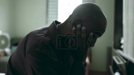 Photo for Close-up face of depressed senior struggles with life's challenges in moody gloomy bedroom covering face in shame and regret in somber atmosphere. African American person suffering - Royalty Free Image
