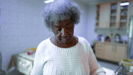 Foto de Una anciana mujer negra sudamericana parada en la cocina cocinando pasta. Gray Haired 80s persona de ascendencia africana preparando el almuerzo - Imagen libre de derechos