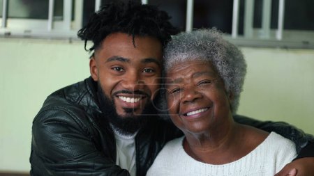 Afroamerikanisch junger Enkel umarmt seine älteren grauen Haare Großmutter Portraitgesichter, die in echt liebevollen Moment in die Kamera schauen, zarter Arm um Schulter, generationenübergreifende Bindung