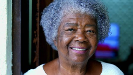 Foto de Una feliz anciana sudamericana negra de 80 años de ascendencia africana sonriendo a la cámara. Retrato de una señora de pelo gris con arrugas y expresión alegre de pie en la casa residencial - Imagen libre de derechos