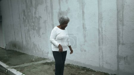 Foto de Anciana mujer negra sudamericana llega a casa desde la calle de la acera, abre la puerta principal de la residencia regresando cerrando la puerta detrás de ella, persona mayor de 80 años de ascendencia africana - Imagen libre de derechos