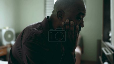 Photo for Close-up face of depressed senior struggles with life's challenges in moody gloomy bedroom covering face in shame and regret in somber atmosphere. African American person suffering - Royalty Free Image