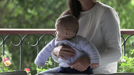 Téléchargez les photos : Mère tenant bébé enfant en bas âge fils par fenêtre - en image libre de droit