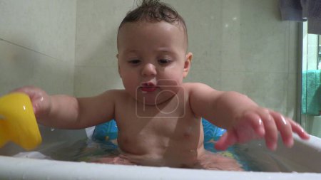 Téléchargez les photos : Bébé enfant dans la baignoire nettoyage avec de l'eau jeu avec jouet - en image libre de droit