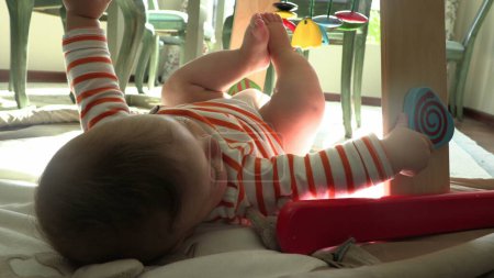 Foto de Lindo bebé sosteniendo los pies con la mano y jugando con juguetes de madera - Imagen libre de derechos