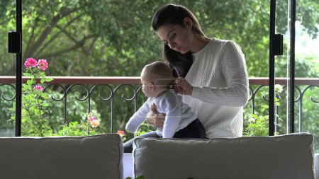 Photo for Candid mother and baby child together next to home window - Royalty Free Image