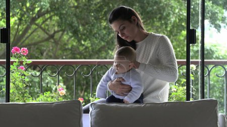 Téléchargez les photos : Candid mère et bébé enfant ensemble à côté de la fenêtre de la maison - en image libre de droit