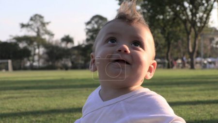 Téléchargez les photos : Bébé enfant mignon au parc extérieur pendant le coucher du soleil regardant vers le haut à la découverte - en image libre de droit